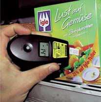 Hand hält schwarzes Handgerät mit Display vor Verpackungen mit Gemüse- und iglo-Aufdruck im Regal